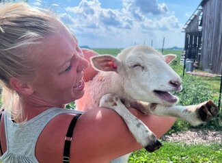 A woman smiles holding a baby goat