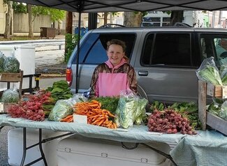 A young girl poses in behind a farmer's market stand