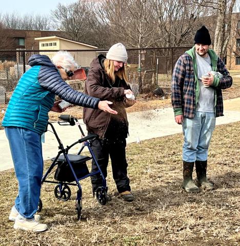 Phyllis Brussell spreads prairie seeds from her walker with Skye Silver and Stephen Schilling.