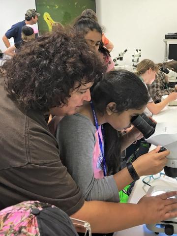 teacher helping girl use microscope