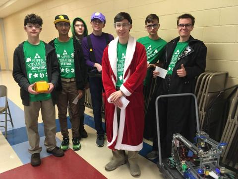 7 teens standing with their robot. One is wearing a red and white robe, one is in a purple shirt.