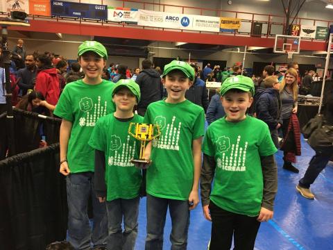 4 young boys in green hat and shirt holding trophy.