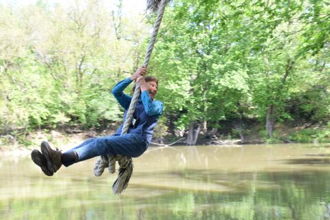 woman swinging on rope swing out above water
