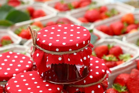 Jars of strawberry jam with red and while polka dot cover. Strawberries in the background.