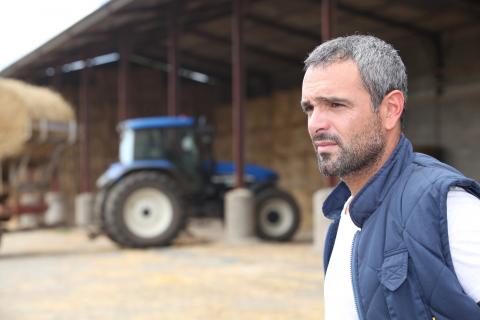 Man with gray hair wearing a blue vest. Blue tractor in the background.