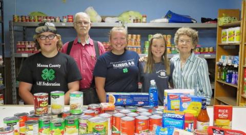 4-H teens and adult volunteers standing in food pantry with food displayed on counter