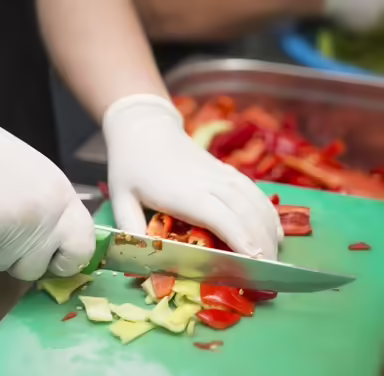 Gloved hands cutting vegetables