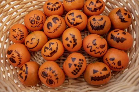 Wicker basket with clementine fruits. Each fruit has a different Halloween themed face drawn on it.