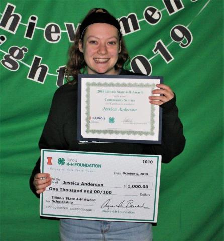 Teen girl holding check and award with a green backdrop.