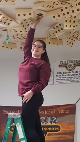 Teenage girl with glasses hanging target pages on the ceiling.