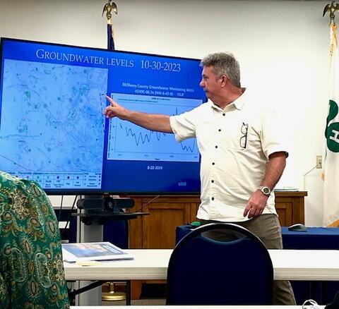 A man in a classroom points to a screen showing groundwater levels