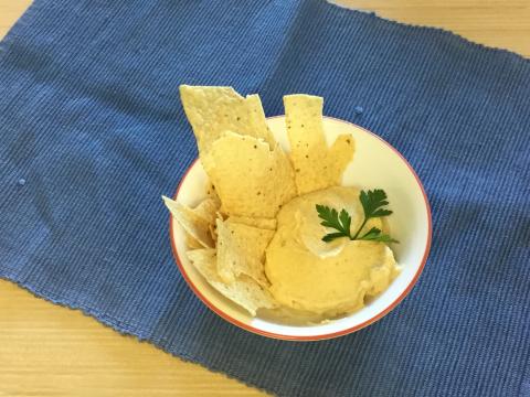 Yellow split pea hummus dip with tortilla chips on blue background