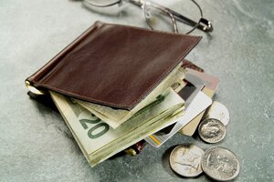 A brown wallet with a $20 bill and some coins in front of a pair of glasses