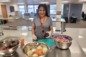 A woman smiling holding a potato while making a recipe in an industrial kitchen.