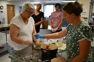 An instructor tells a participant in the class how to put the lid on a jar of marmalade as other class participants watch in the background.