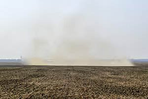A large dust storm picking up while traveling across a farm field