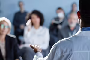 Group of adults sitting down facing front of room while listening to a speaker
