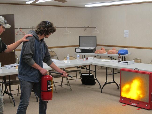Teen practicing putting out a simulated fire with a fire extinguisher 