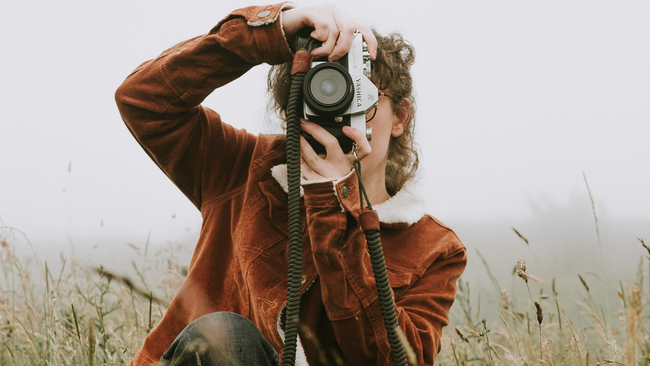 woman with brown hair taking photograph in nature with camera