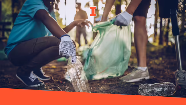 A woman bending down picking up trash while a man holds the garbage bag open.