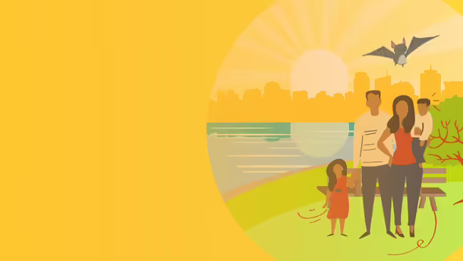 A family sits on the river bank with a city in the background.  A bat flies over head