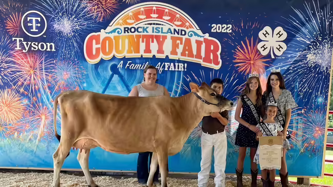 4-H members standing in front of fair sign with a cow
