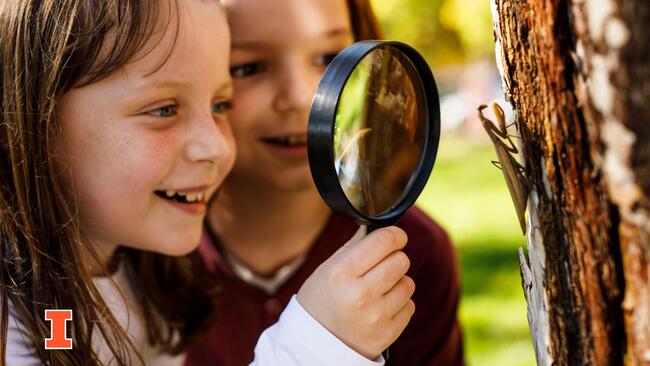 Two girls looking at an insect through a magnifying glass