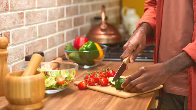 Hands cutting vegetables on cutting board in kitchen