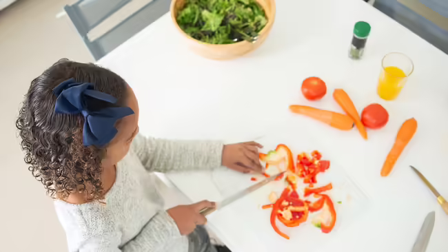 A young girl cutting vegetables on a cutting board.