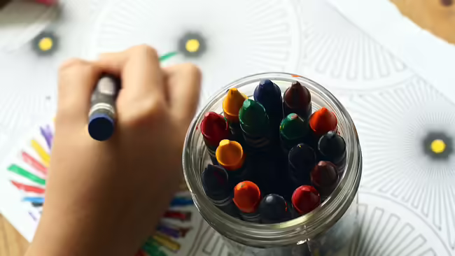 a child's hand holding a crayon with a jar of crayons next to it
