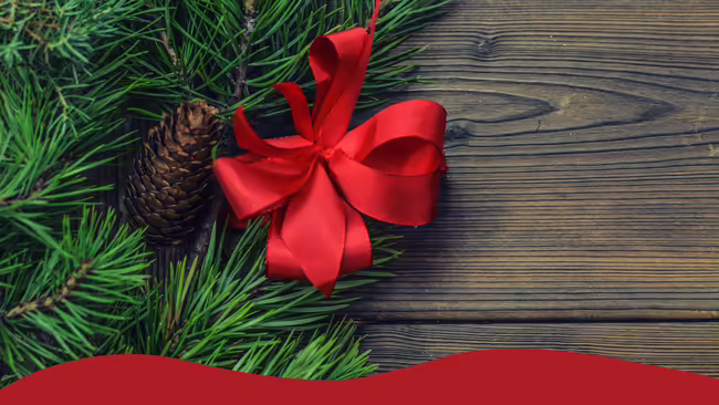 Red ribbon tied into a bow laid on pine branches on a wooden backgraound.