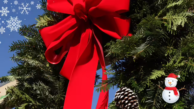 An evergreen wreath with pinecones a red ribbon bow on the top with a snowman and snowflakes.