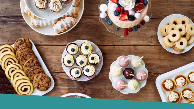 A table with cake, pie, cookies, cake pops, cupcakes, and other various desserts.