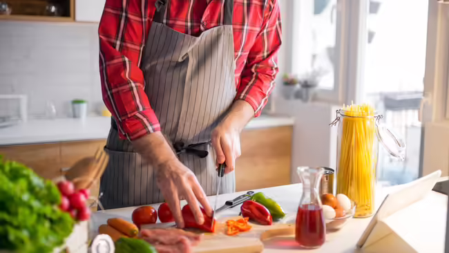 Person at kitchen counter slicing vegetables.