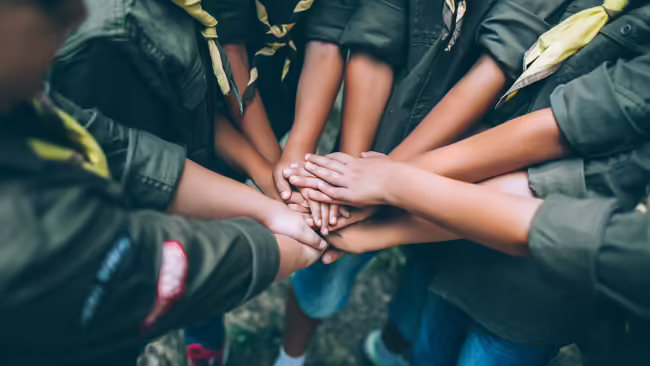 Boy Scouts stand with their hands together in a circle to do a team cheer.