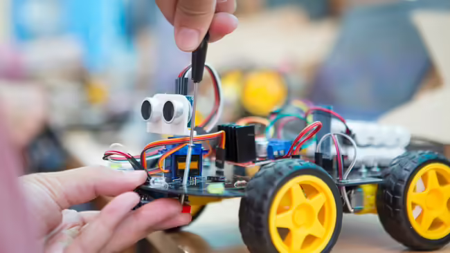 Youth hands work with a screw driver to build a robot.