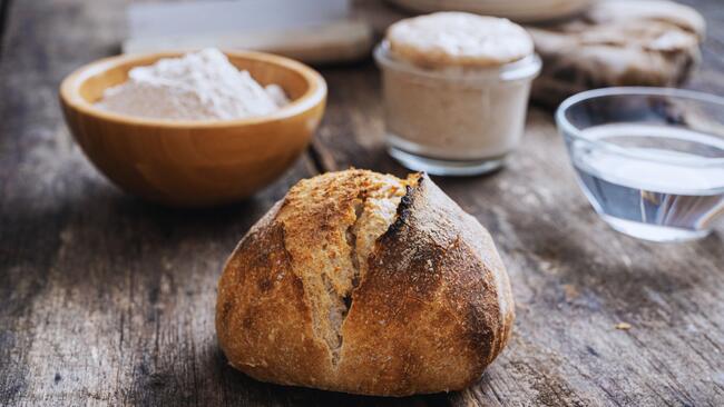 Table with sourdough loaf, starter, flour, and water pictured