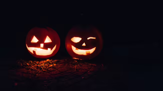 Two lighted jack-o-lanterns sit in the dark.