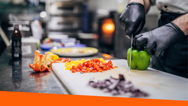 A chef cutting a green pepper on a cutting board with a variety of vegetables that are cut surrounding the cutting board.