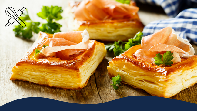 Savory puff pastries sitting on a wooden table with ham on top of the pastry.