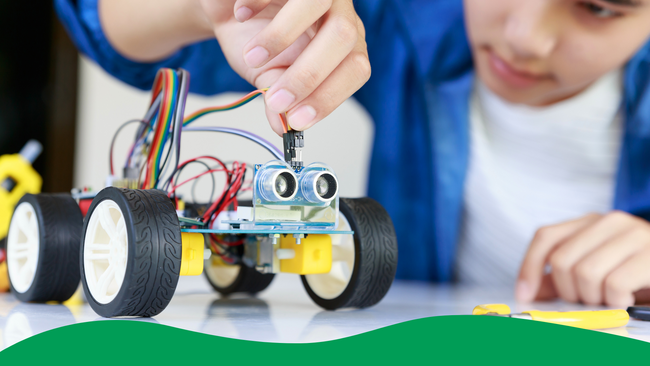 A young teen plugging cables into a robotic toy car.