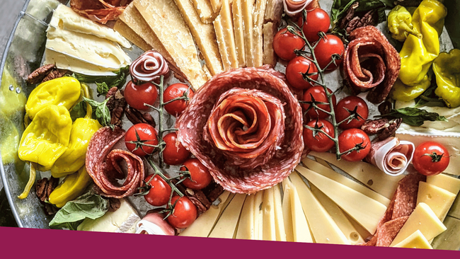 A charcuterie board with different meats, cheeses, and vegetables displayed nicely on a metal tray/