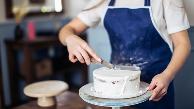 person in blue apron icing a cake on a stand