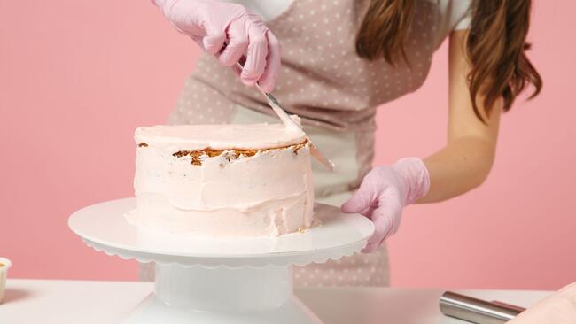 Chef with apron and pink gloves icing a cake on a stand