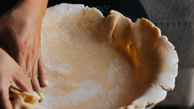 two hands pressing a pie crust into a dish