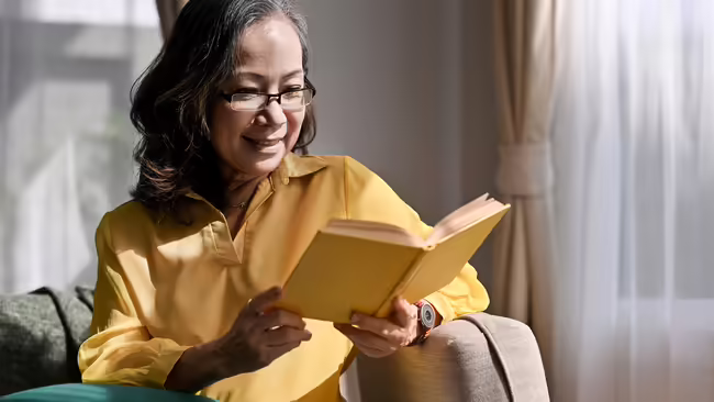 Senior women reading a book in a living room.