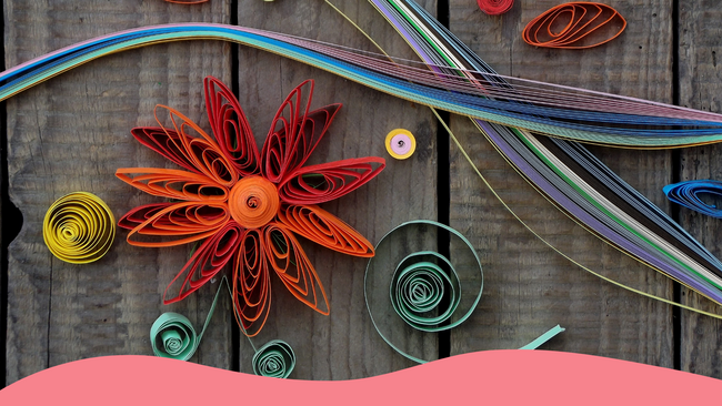 A quill paper flower and other designs on a wooden background.