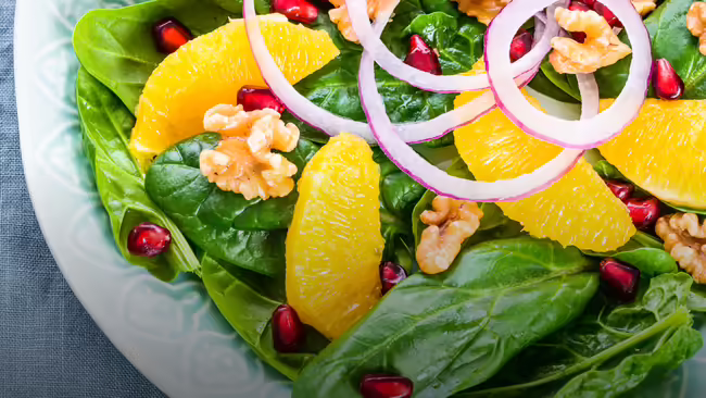 A salad with vegetables and fruits in a white bowl.