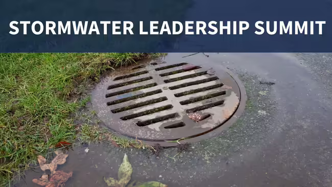 A close-up image of a circular storm drain grate surrounded by grass, pavement, and fallen leaves, with "STORMWATER LEADERSHIP SUMMIT" text displayed across the top of the image on a dark blue overlay.