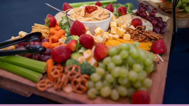 board includes a variety of cheeses, fruits, vegetables, dips and crackers.